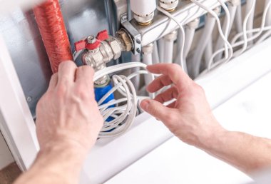 Eller, çeşitli borulara bağlı bir vanayı ayarlayan bir tesisat sistemi üzerinde çalışıyor..