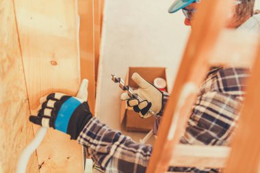 Bir işçi, gün ışığında bir şantiyede ahşap tahtalar üzerinde matkap kullanıyor..