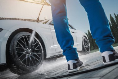 Bir insan evde gün ışığında araba tekerleklerini temizlemek için basınç makinası kullanır. Araç Bakım TemasıName.