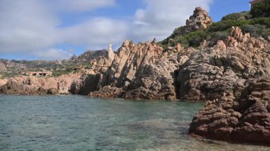 İnsanlar Sardunya kıyısında yürürken dalgalar kayalara çarpar..