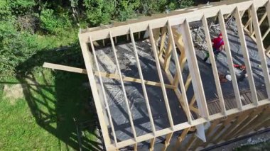 İşçiler gün ışığında ormanlık bir alanda ahşap bir çerçeve inşa ediyorlar. Araçlar ve malzemeler görünür..