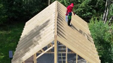 Bir insan gün ışığında ormandaki bir binanın ahşap çatısında çalışır..