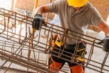 Sarı şapkalı bir işçi, gün ışığında inşaat için hazırlanırken çelik parmaklıkları tutuyor..