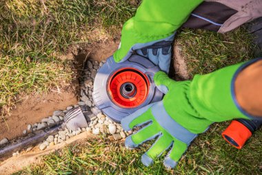 Bir kişi bahçe sulama sisteminin bir parçasını tamir ediyor..