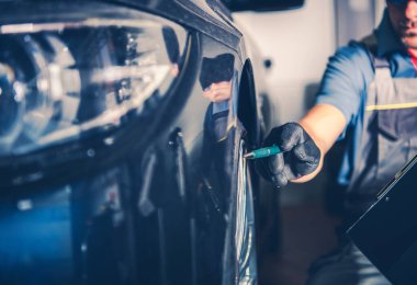 Bir teknisyen atölyede bir araba üzerinde çalışıyor, lastiği ya da tekerleği kontrol ediyor..