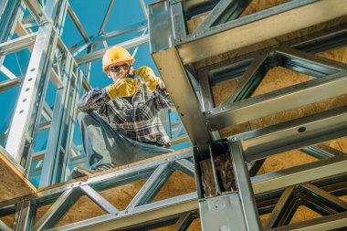 Bir işçi metal bir iskelet üzerinde otururken malzemeyi kesiyor.