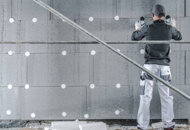 İşçi inşaat halindeki bir binanın duvarına yalıtım panelleri kurmak için araçlar kullanıyor.