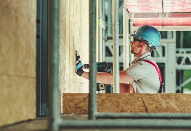 Bir işçi öğleden sonra güneşli bir inşaat sahasında duvar örüyor..