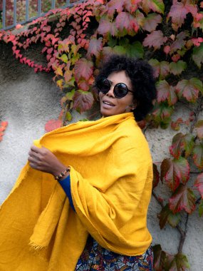 Sonbahar yapraklarının önünde duran zarif bir Afrikalı Amerikalı kadının dikey portresi.