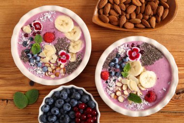 Yaban mersinli meyve suyu kasesi, üzümlü üzümlü, chia tohumlu, muz ve bademli ahşap zemin. Üst görünüm.