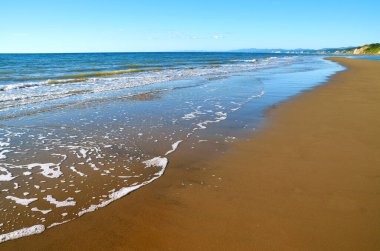 Sarı kumlu güneşli yaz plajı ve gün boyunca sakin turkuaz deniz..