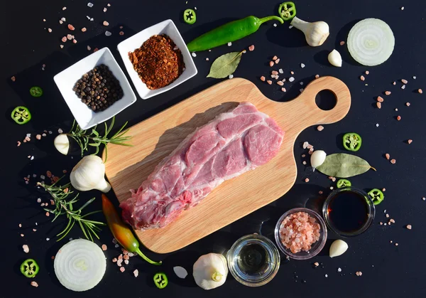 Mat bakgrund. Köttet på en skärbräda och peppar, lagerblad, rosmarin, lök, Himalaya salt, olivolja, soja på svart bakgrund. Mallen för visning av produkter — Stockfoto
