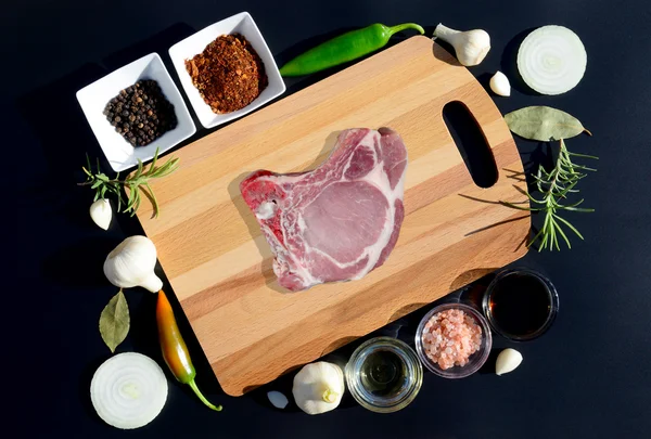 Мясо стейк на разделочной доске и перец, лавровый лист, розмарин, лук, соль, оливковое масло, соевый соус на черном фоне — стоковое фото