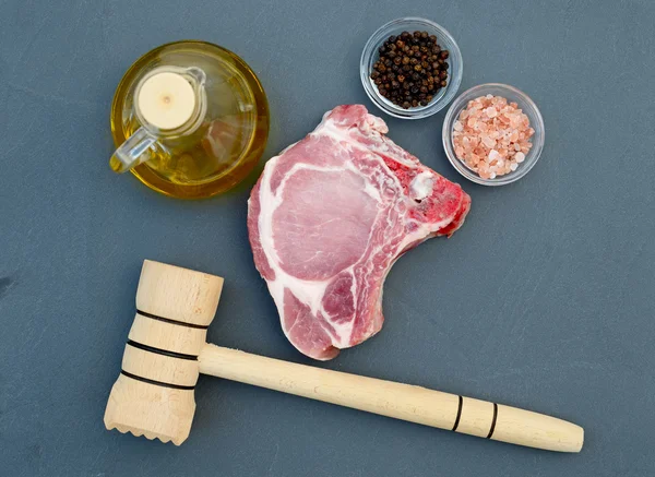 Steak de viande fraîche sur le dessus de table en pierre naturelle. À côté de la viande avec sel, poivre, huile d'olive et marteau à viande en bois — Photo