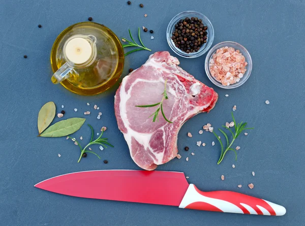 Frischfleisch auf der Tischplatte aus Naturstein. neben dem Fleisch mit Salz, Pfeffer, Olivenöl, Lorbeerblatt, Rosmarin und einem Messer zum Schneiden — Stockfoto