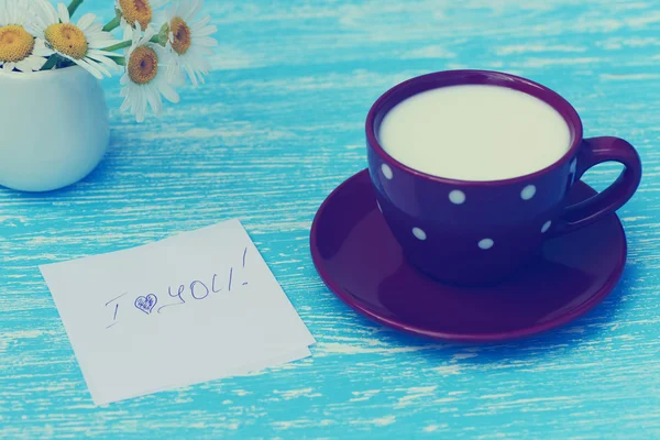 Flores Margarida e xícara de leite com eu amo você nota no fundo de madeira azul rústico. Foto em estilo vintage — Fotografia de Stock