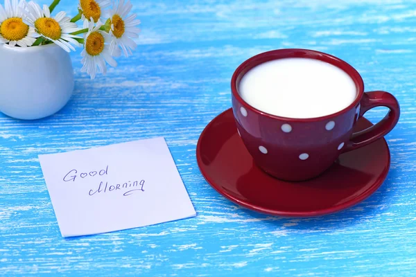 Daisy bloemen en kopje melk met opmerking Goedemorgen op rustieke blauwe houten achtergrond — Stockfoto