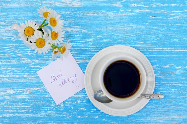 Daisy bloemen en een kopje thee met opmerking Goedemorgen op rustieke blauwe houten achtergrond — Stockfoto