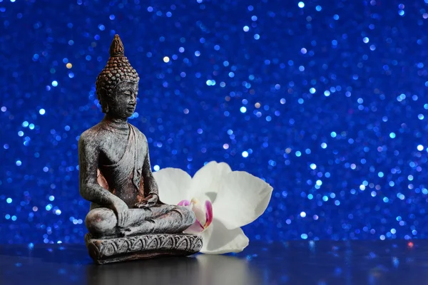 Статуя Будды и цветок орхидеи на ярком блестящем фоне с боке — стоковое фото