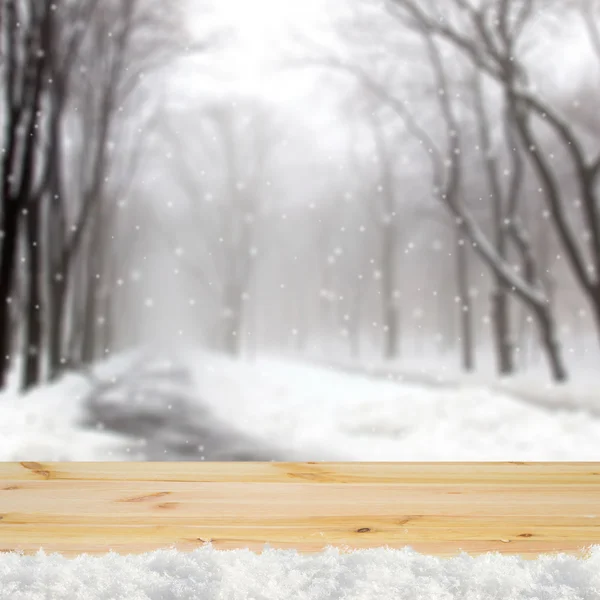 Blurred winter background with snow covered forest and shabby table — Stock fotografie