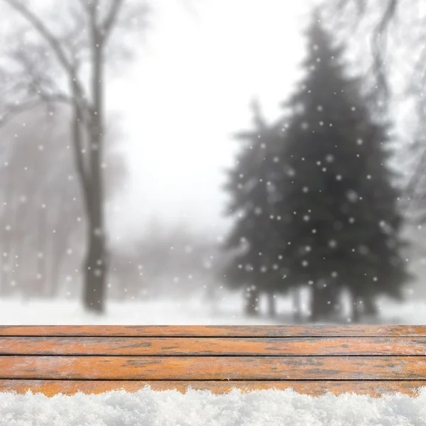 Blurred winter background with snow covered forest and shabby table — Stock fotografie