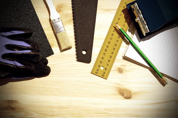 Workplace and tools of a carpenter or builder.Hand saw, ruler, brush, notebook, pencil, sandpaper, and work gloves.Special toned photo in vintage style — ストック写真