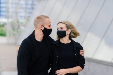 Karantina sırasında şehrin boş sokaklarında yürüyen şık koruyucu maskeler takan bir çift..