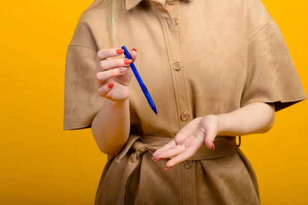 Blue pen in woman hand isolated on a yellow background.