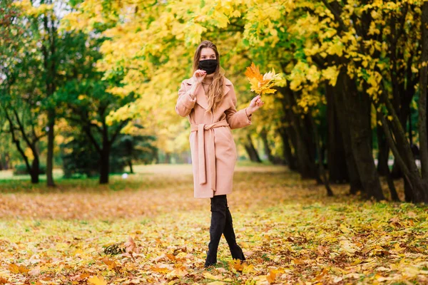 A young woman protecting from corona virus when walking in park. Autumn background.