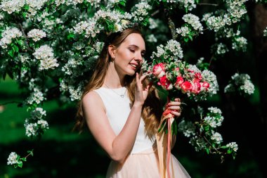 Beyaz gelinlikli gelin yeşil parkta bir buket tutuyor. Güneşli bir günde yaz düğünü..