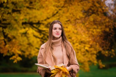 Güzel bir kadın sonbahar mevsiminde parkta vakit geçiriyor.