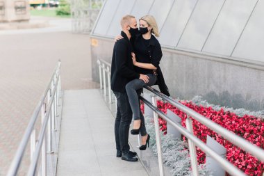 Coronavirus salgını karantinası sırasında Avrupa şehrinin boş sokaklarında gezen modaya uygun koruyucu maskeler, kot ceketler giyen çift.