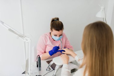 Güzellik salonunda kadın manikür ustası müşterinin elleriyle çalışıyor.