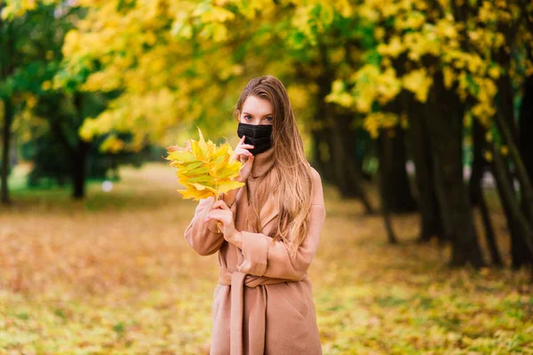 一个戴着医用面罩的年轻美丽女子在秋天背景下的画像 — 图库照片