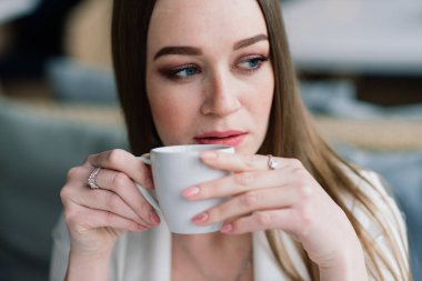 Beyaz ceketli genç bir kadın kafeteryada çalışıyor, kahve içiyor.