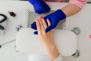 Güzellik salonunda kadın manikür ustası müşterinin elleriyle çalışıyor.