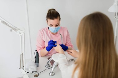 Güzellik salonunda kadın manikür ustası müşterinin elleriyle çalışıyor.