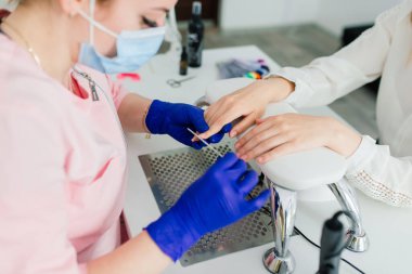 Güzellik salonunda kadın manikür ustası müşterinin elleriyle çalışıyor.