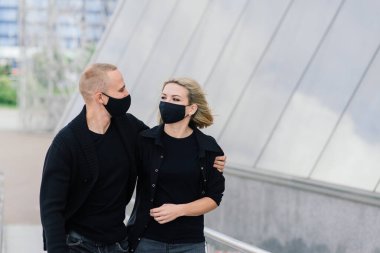 Karantina sırasında şehrin boş sokaklarında yürüyen şık koruyucu maskeler takan bir çift..