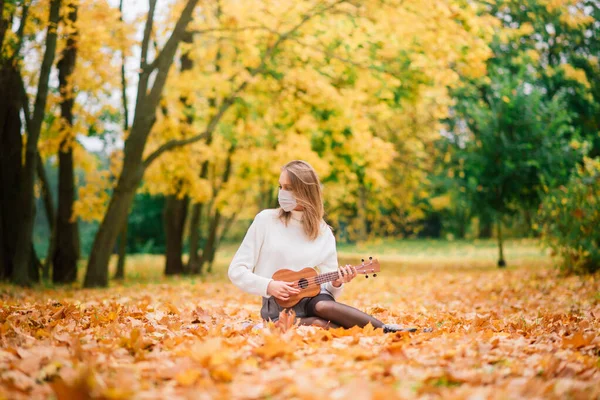 秋の公園でウクレレギターを演奏保護マスクの肖像若い女性 ライフスタイル健康旅行のコンセプト — ストック写真