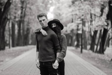 Genç kızıl saçlı kadın, sonbahar parkında genç bir adamla yürürken maske takıyor..