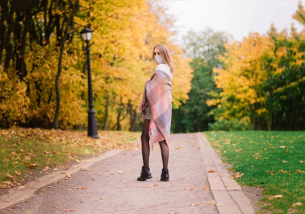 A young woman protecting from corona virus when walking in park. Autumn background.