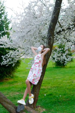 Yalnız genç kız çiçek açan bir bahçede virüs ve alerjiye karşı koruyucu maske takıyor.
