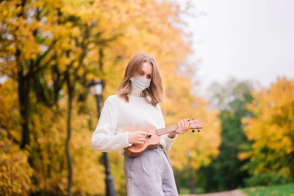 마스크를 공원에서 우쿨렐레 기타를 연주하는 여성의 초상화 — 스톡 사진