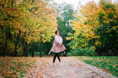 Altın sonbahar parkında sivri ayakkabılarla dans eden kadın balerin, sarı yaprakların üzerinde bale pozu veriyor.