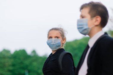 Okul çocukları, sağlık maskeli kız ve erkek çocuklar şehir parkında yürüyor..