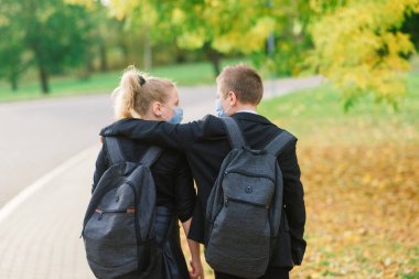 Okul çocukları, sağlık maskeli kız ve erkek çocuklar şehir parkında yürüyor..