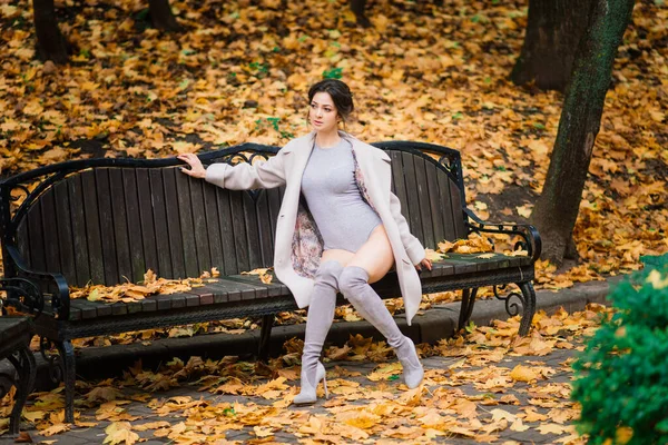 若い美しい黒髪の女性は ランジェリー姿と秋の公園で古典的なコートを身に着けています — ストック写真