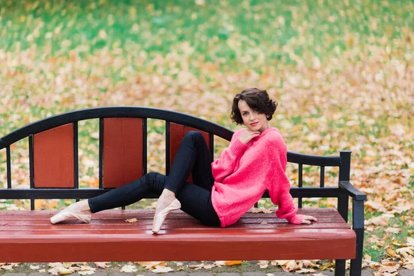아름다운 발레리나의 코트와 구두를 벤치에 공원의 야외에서 휴식을 취하는 — 스톡 사진