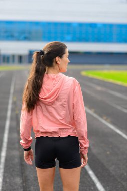 Stadyumda kollarını açarak ısınan sağlıklı genç bir kadın parkta koşu yapıyor..